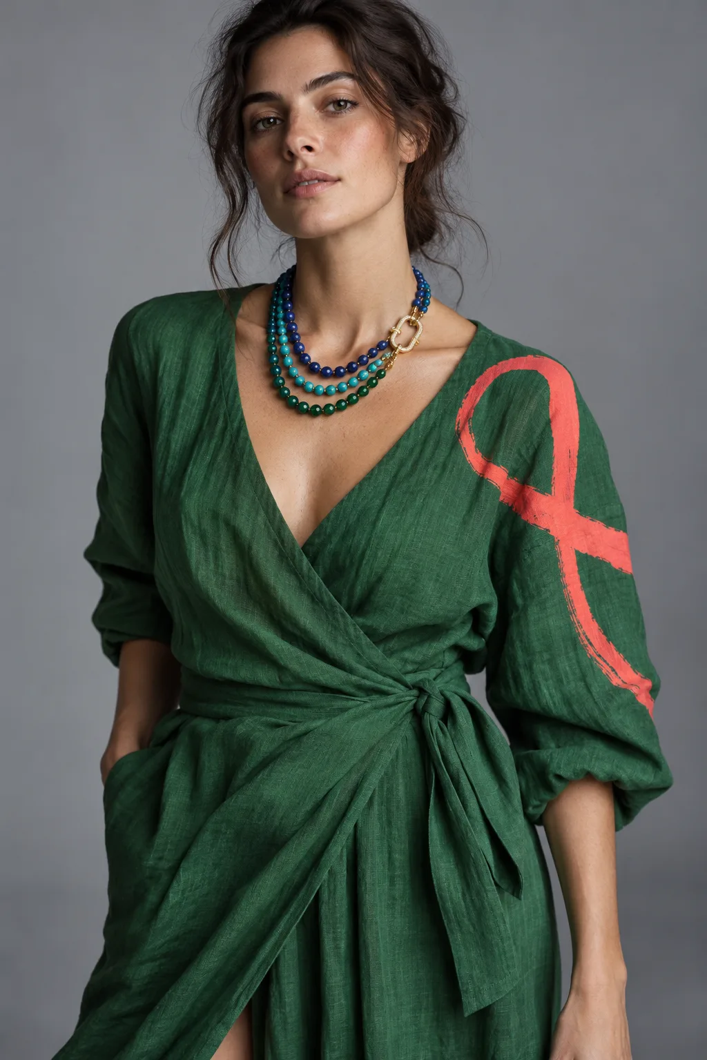 Concept render of a woman in a forest green linen wrap dress with a brushed coral loop painted on the sleeve, wearing layered lapis, turquoise and green strands on a pavé clasp