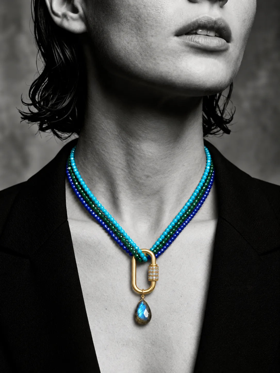 Black and white portrait wearing turquoise, emerald and lapis strands on a gold pavé carabiner with a labradorite drop